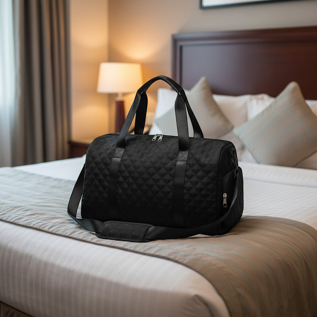 Sac de voyage MoveLite AMOURIA noir matelassé avec bandoulière posé sur un lit d'hôtel