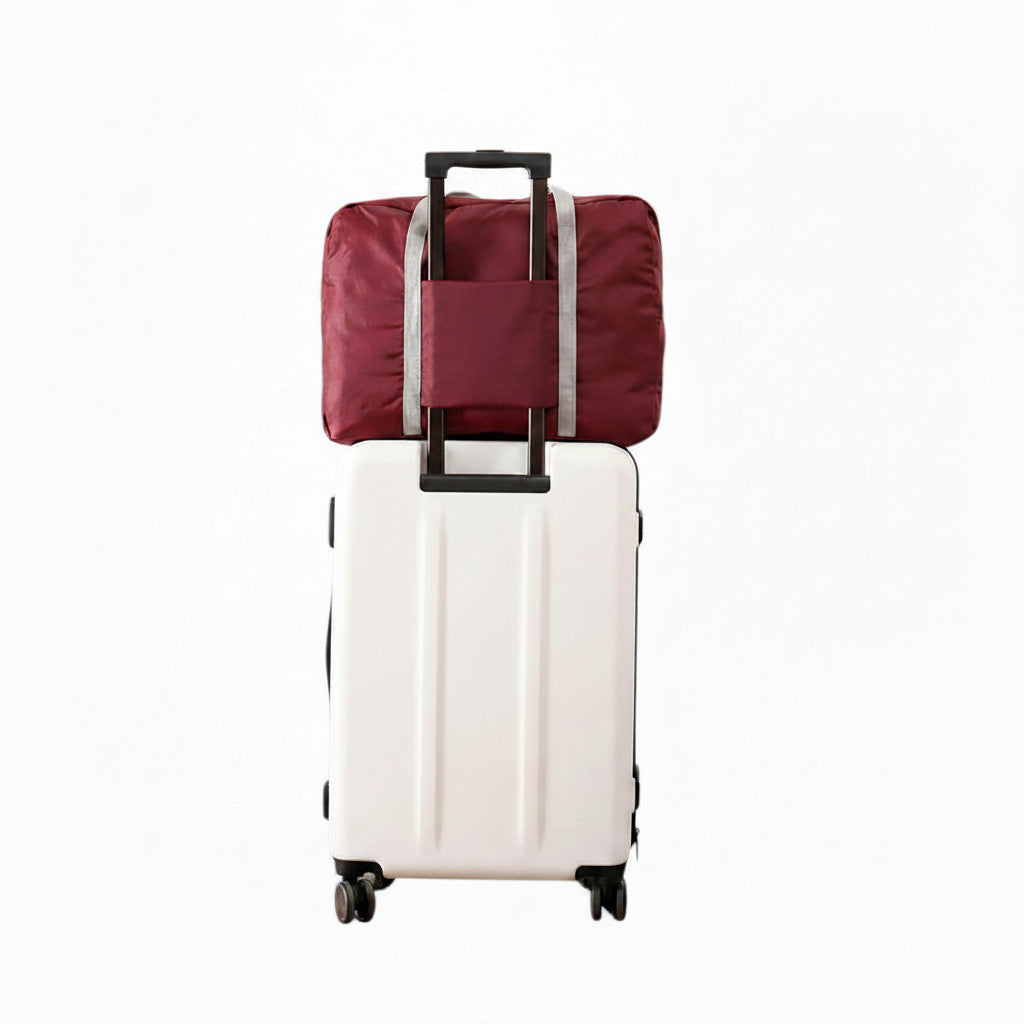 Sac de voyage pliable bordeaux MoveLite fixé sur une valise blanche à roulettes pour le transport