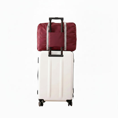 Sac de voyage pliable bordeaux MoveLite fixé sur une valise blanche à roulettes pour le transport