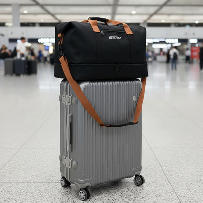 Sac de voyage MoveLite Wanderelle noir avec anses et bandoulière marron posé sur une valise rigide grise à l'aéroport