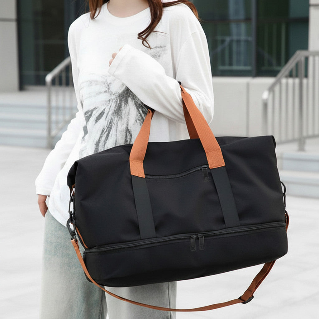 Sac de voyage MoveLite noir avec anses et bandoulière contrastantes orange, porté à l'épaule par une femme