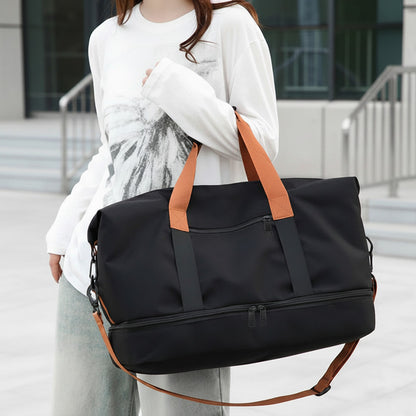Sac de voyage MoveLite noir avec anses et bandoulière contrastantes orange, porté à l'épaule par une femme