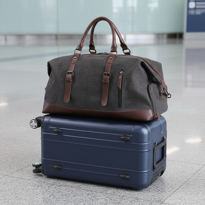 Sac de voyage MoveLite gris en toile avec détails en cuir marron posé sur une valise rigide bleue dans un aéroport